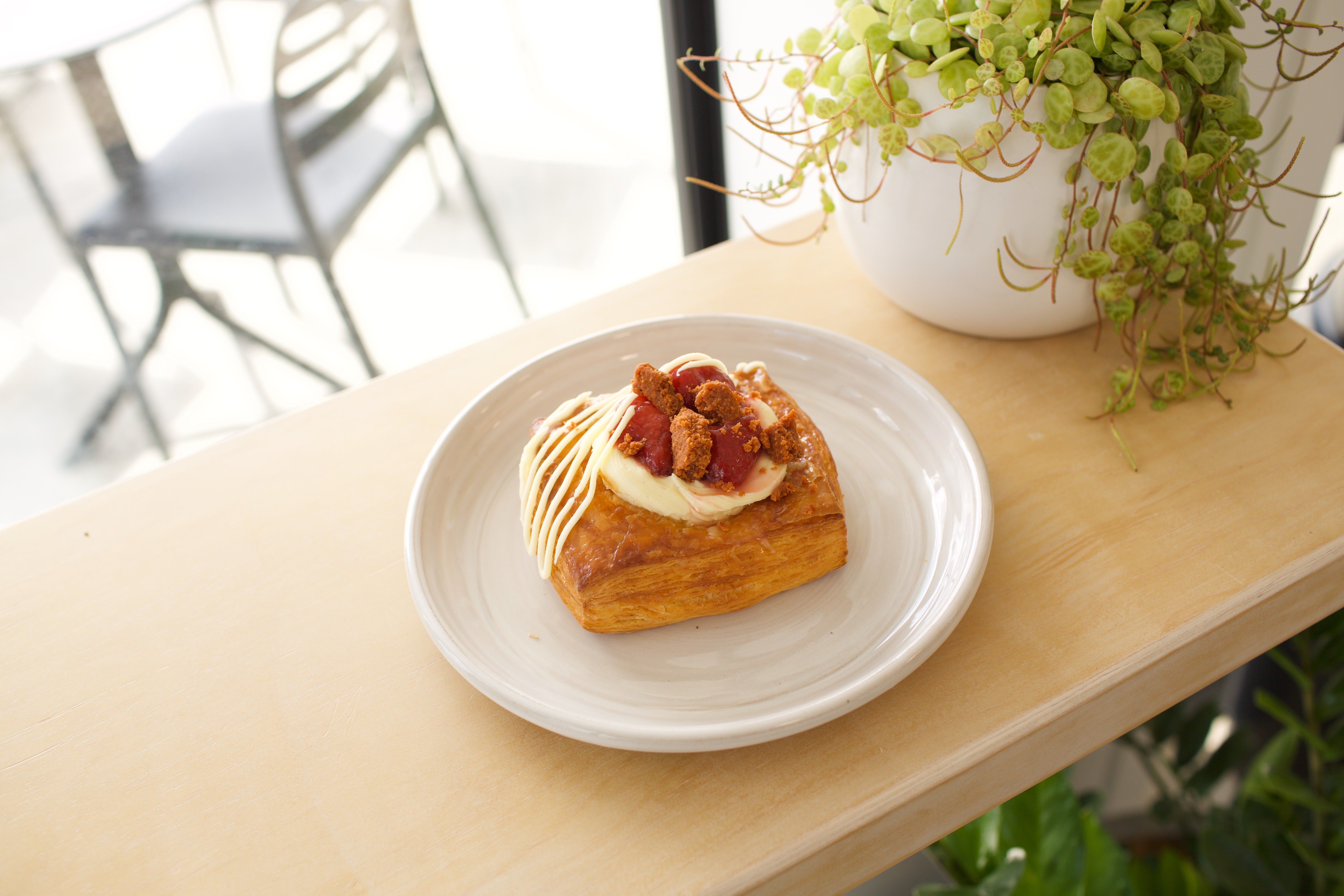 Strawberry White Chocolate Cheesecake Danish on a white plate beside a pot plant