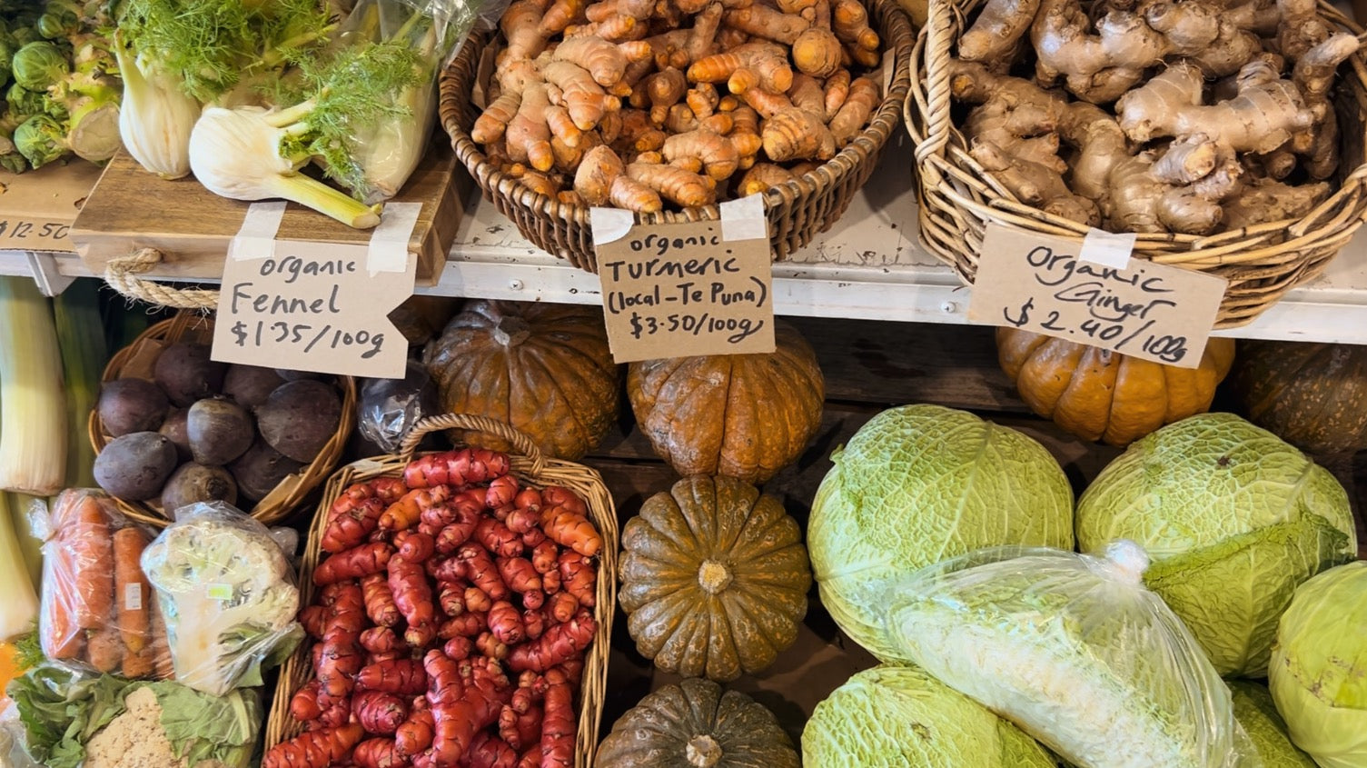 Assorted vegetables including ginger, turmeric, and cabbages displayed in baskets with price tags.