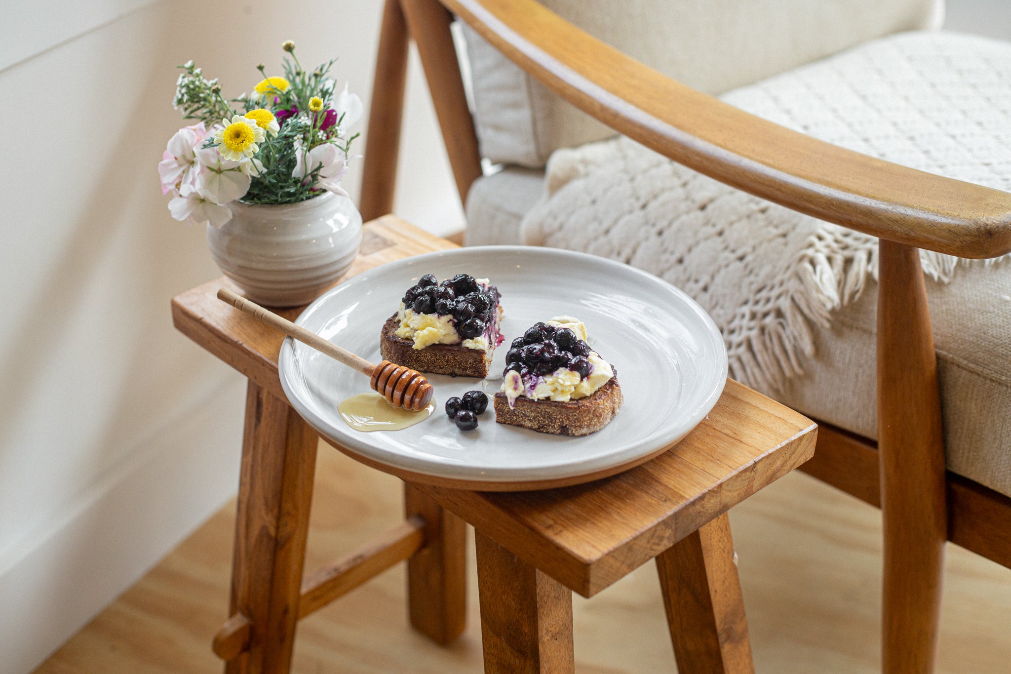 Plate of Fig & Walnut Sourdough French Toast on a small wooden table with a chair and flowers in the background