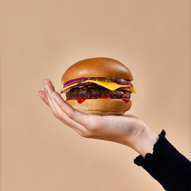 Hand holding a burger against a beige background