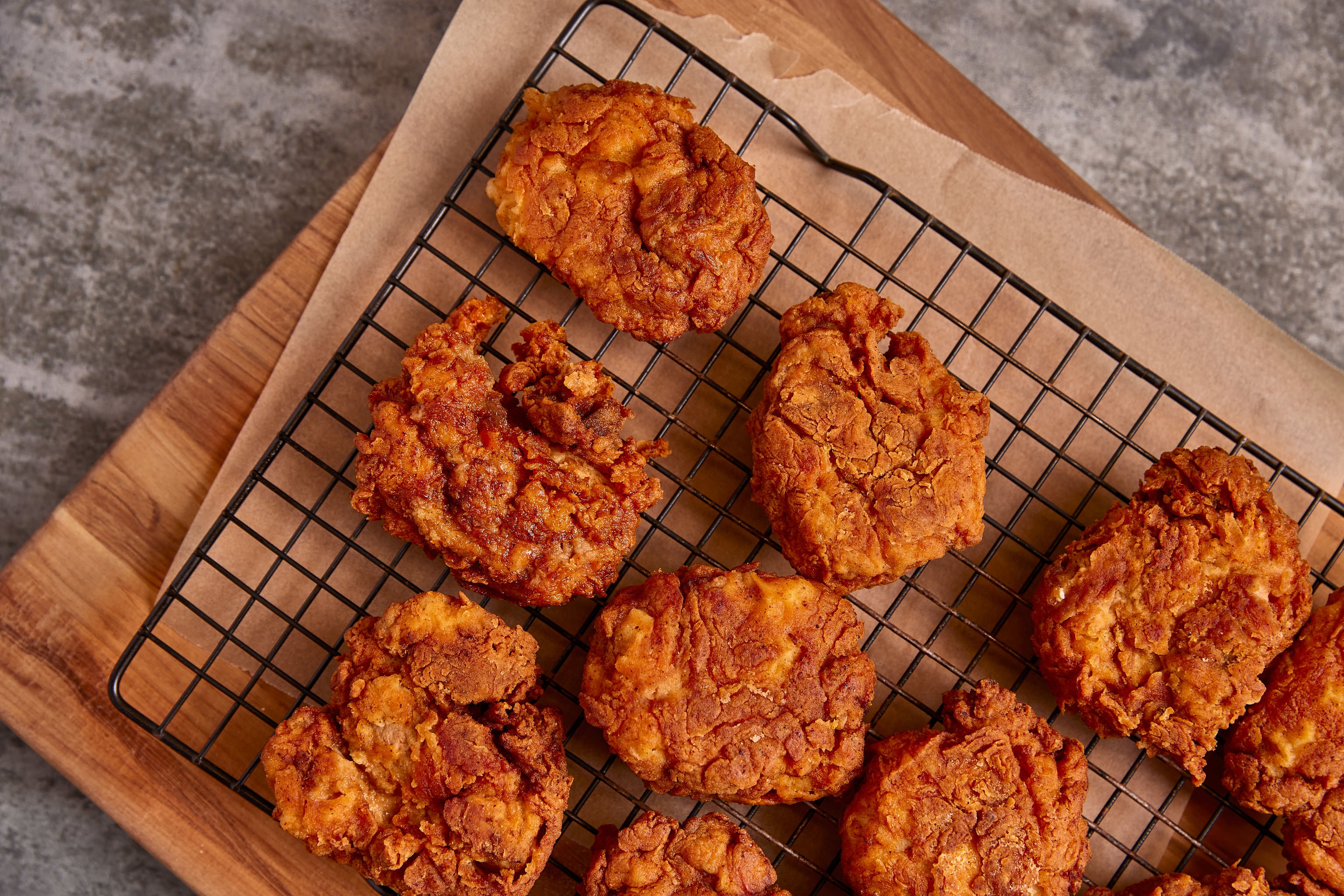 Fried chicken pieces on a cooling rack with a wooden board and gray background
