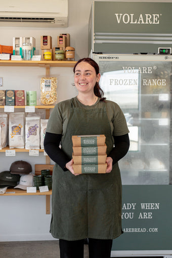 Tyler standing in front of a freezer at Volare Main Bakery store holding a stack of Frozen Sausage Rolls