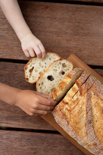 Volare Sliced Sourdough on a wooden chopping board with two small hands grabbing a slice.
