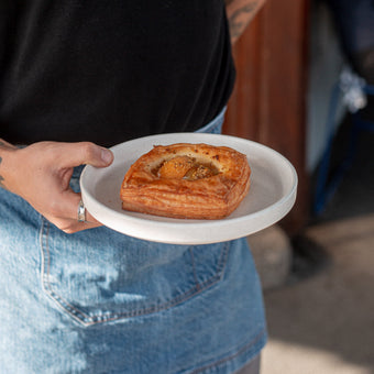 Waiter wearing a denim apron and holding a Volare Apricot & Pistachio Danish