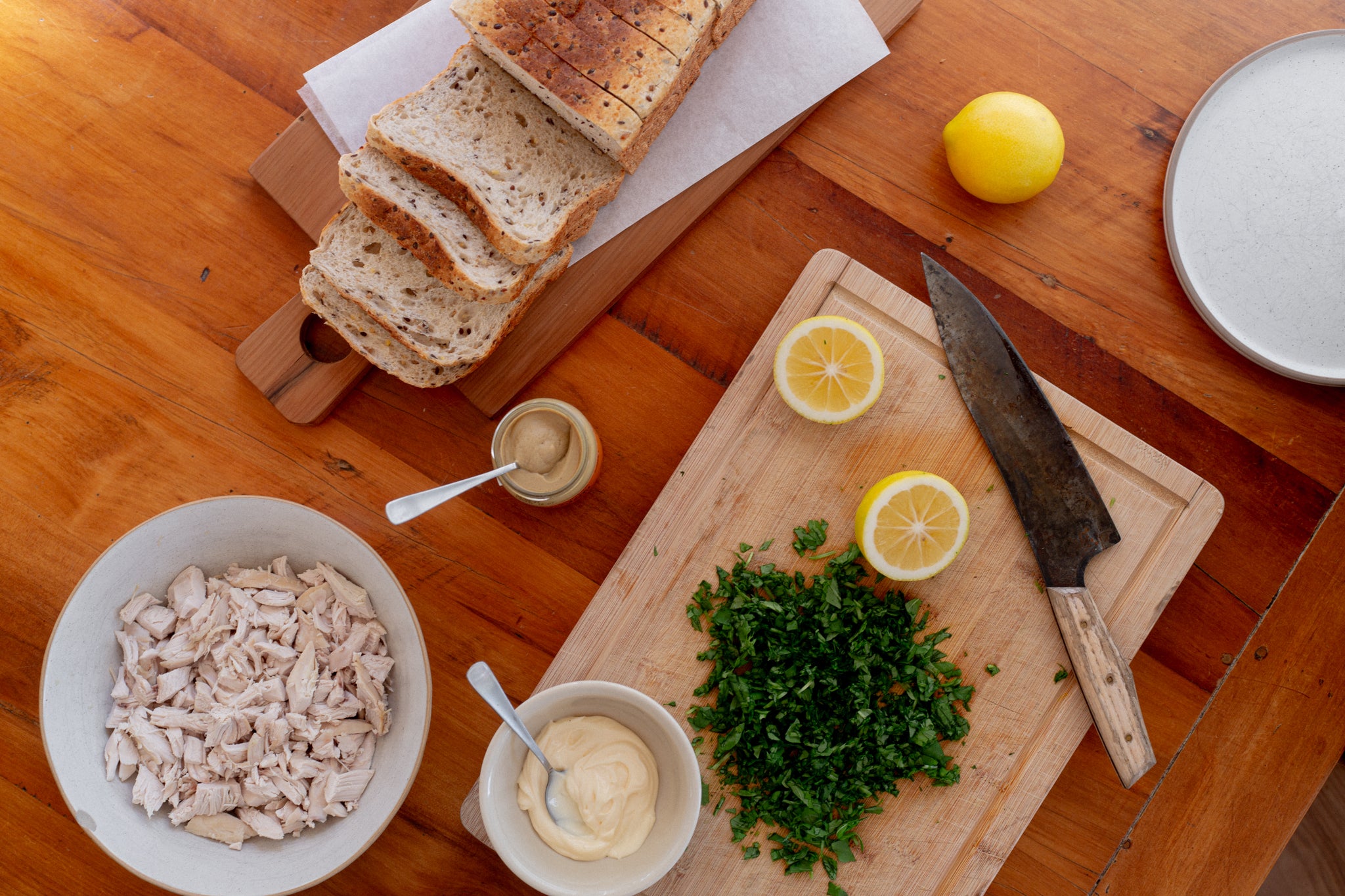 Wooden table with Volare sliced seeded sandwich loaf bread, lemons, herbs, and bowls of ingredients on a wooden surface.