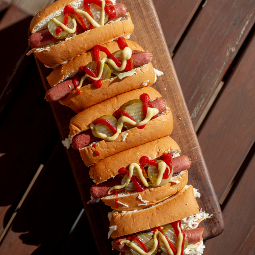 Stack of hot dogs with various condiments on a wooden board