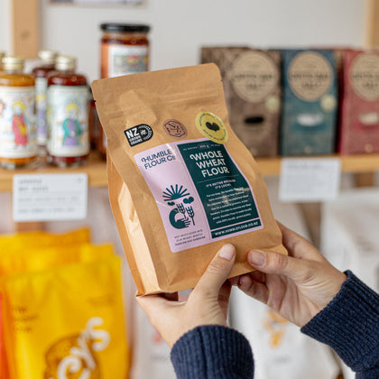Person holding a package of Humble Flour Co. Whole Wheat Flour with a store shelf in the background
