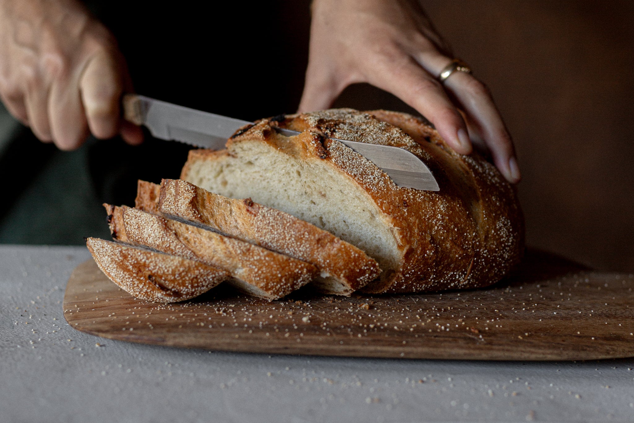 Volare Roast Onion Sourdough being sliced on a wooden cutting board with a bread knife.