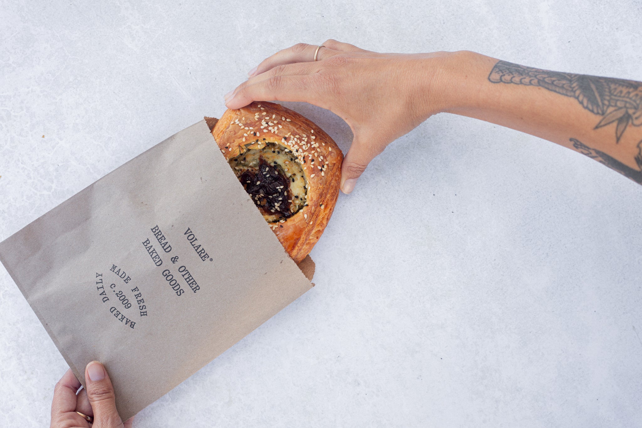 Hand sliding a Volare Balsamic Onion & Ricotta Danish out of a paper bag