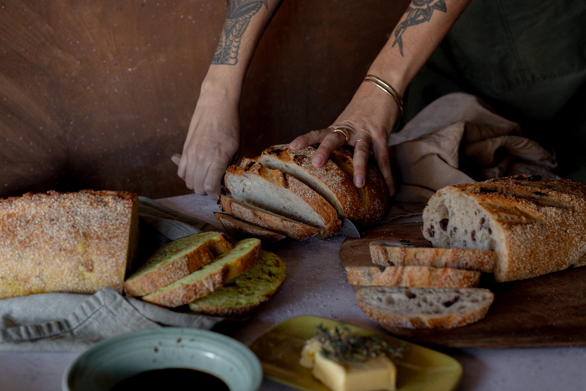 Person slicing Volare bread on a wooden table with various types of unique bread displayed.