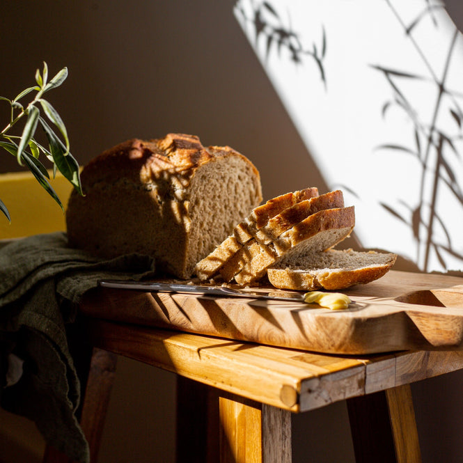 Loaf of PAIN AU LEVAIN and slices on a wooden cutting board with a plant in the background