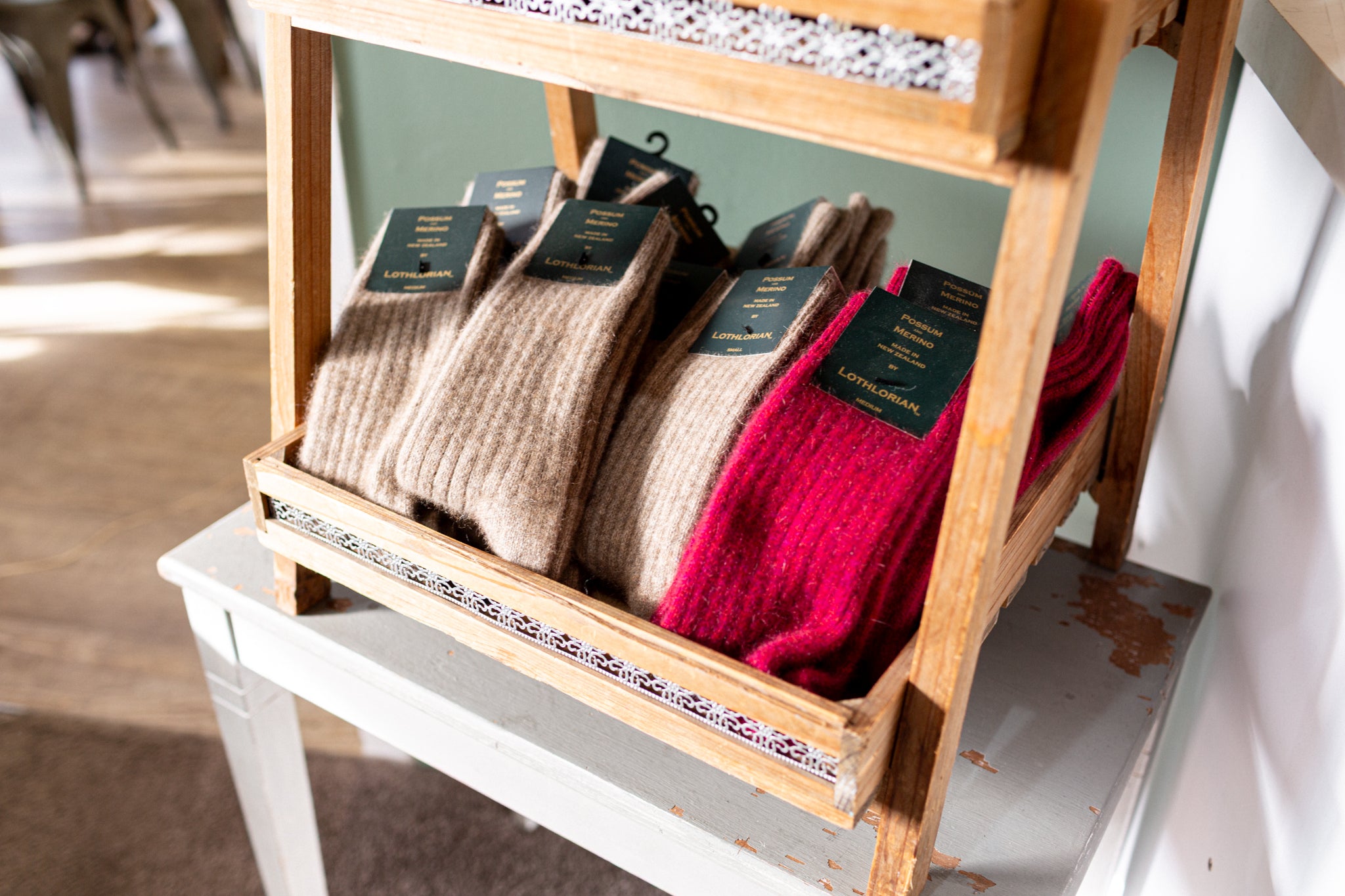 A wooden display shelf holding several pairs of folded ribbed socks, including tan/beige and bright red pairs, each with a black hangtag.