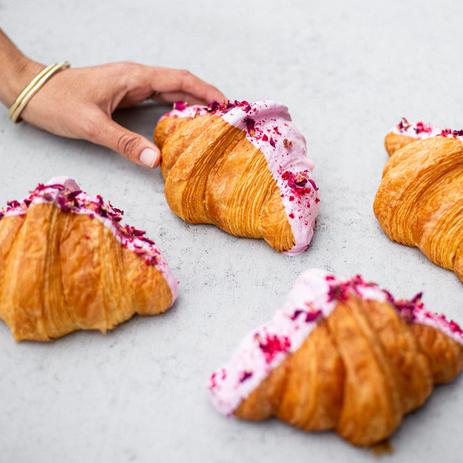 Hand reaching for a croissant with pink icing on a light gray surface