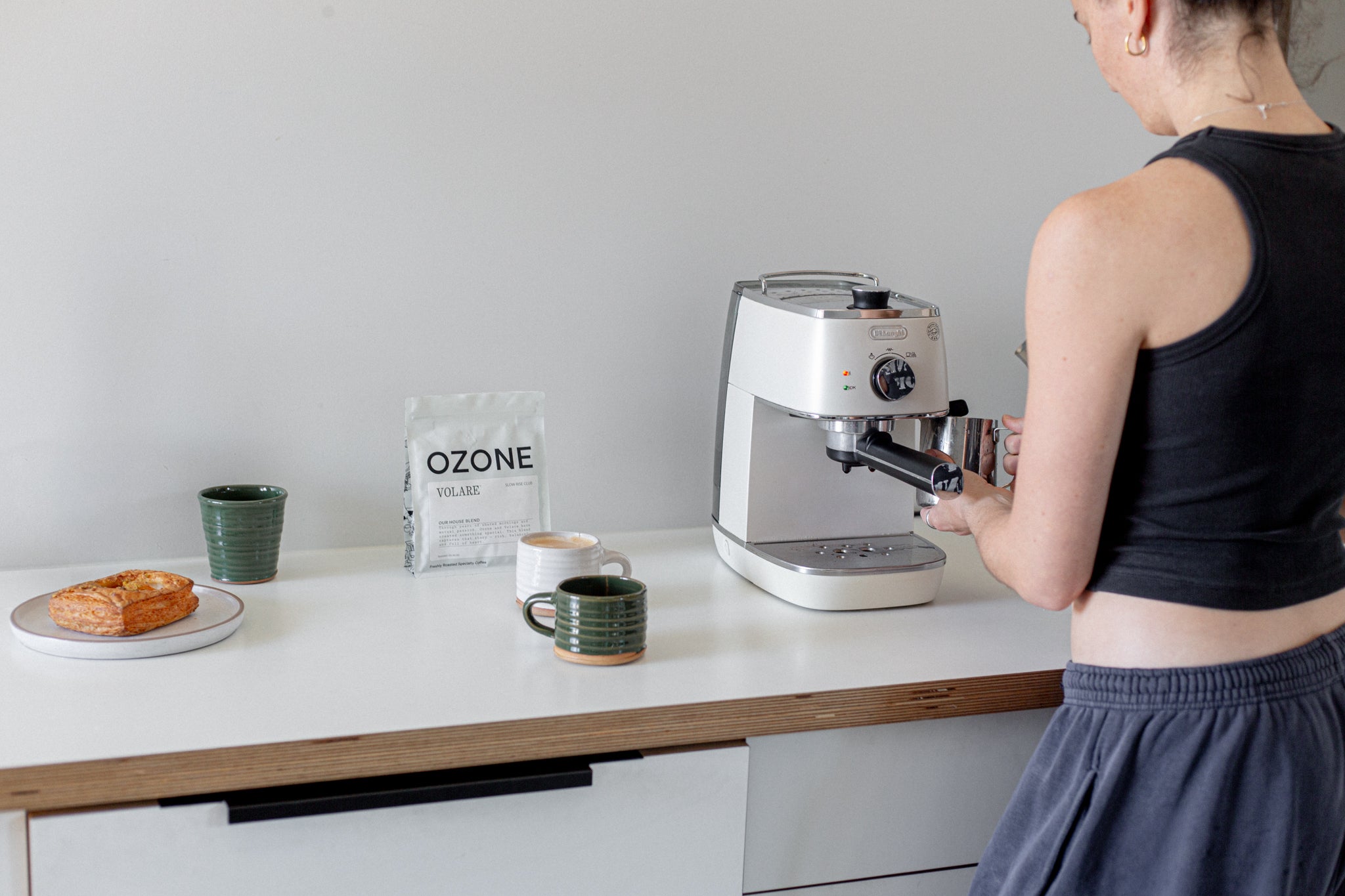 Person using a coffee machine on a kitchen counter with Ozone x Volare coffee in the background.