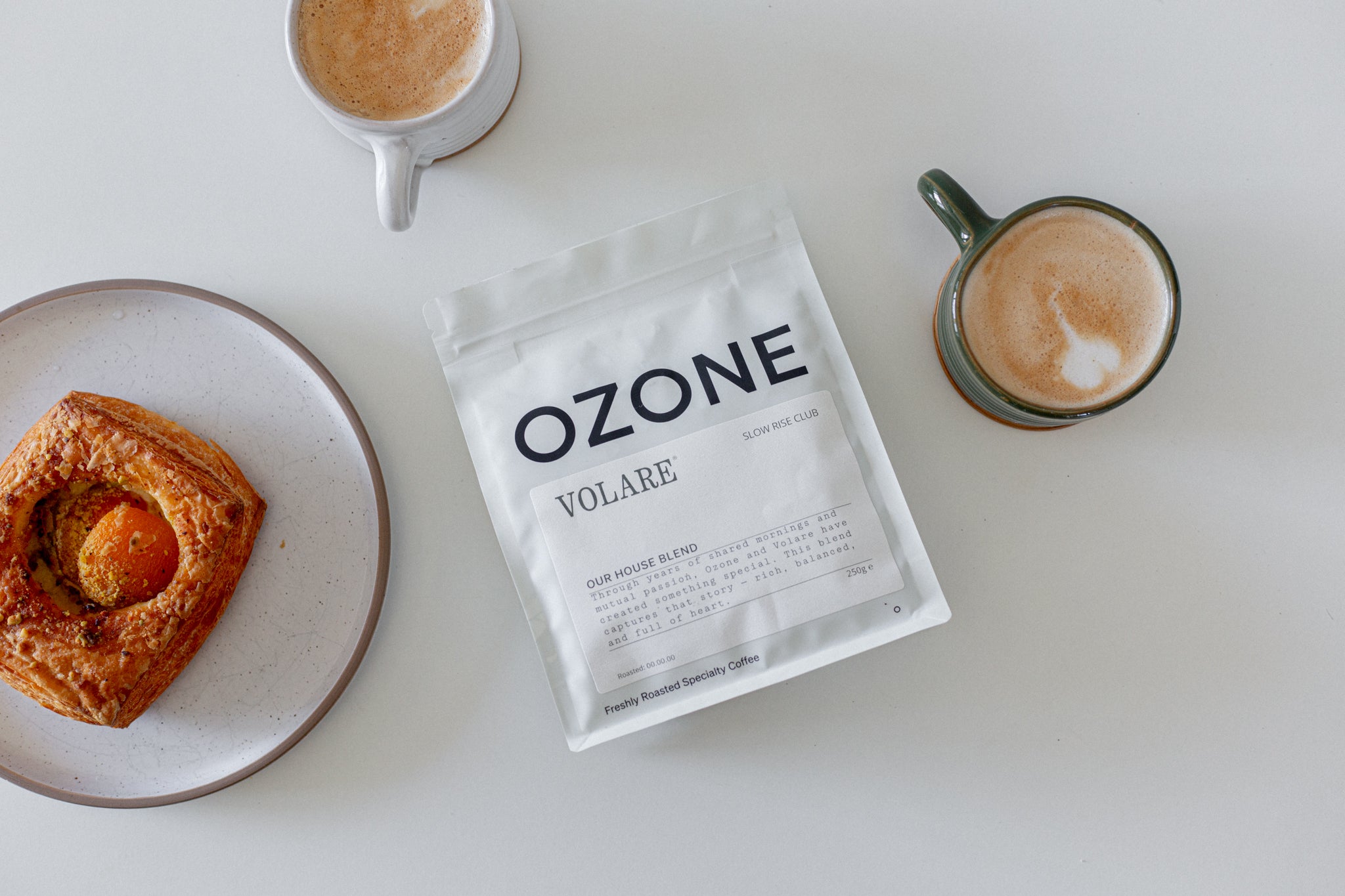 Ozone x Volare coffee package with a croissant and two cups of coffee on a white surface