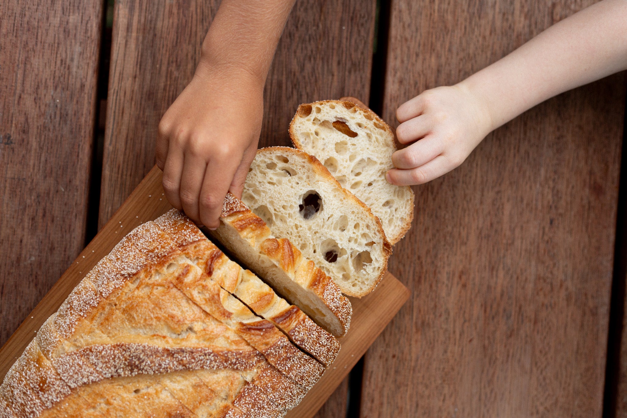 Two small hands reaching for sliced San Francisco loaf
