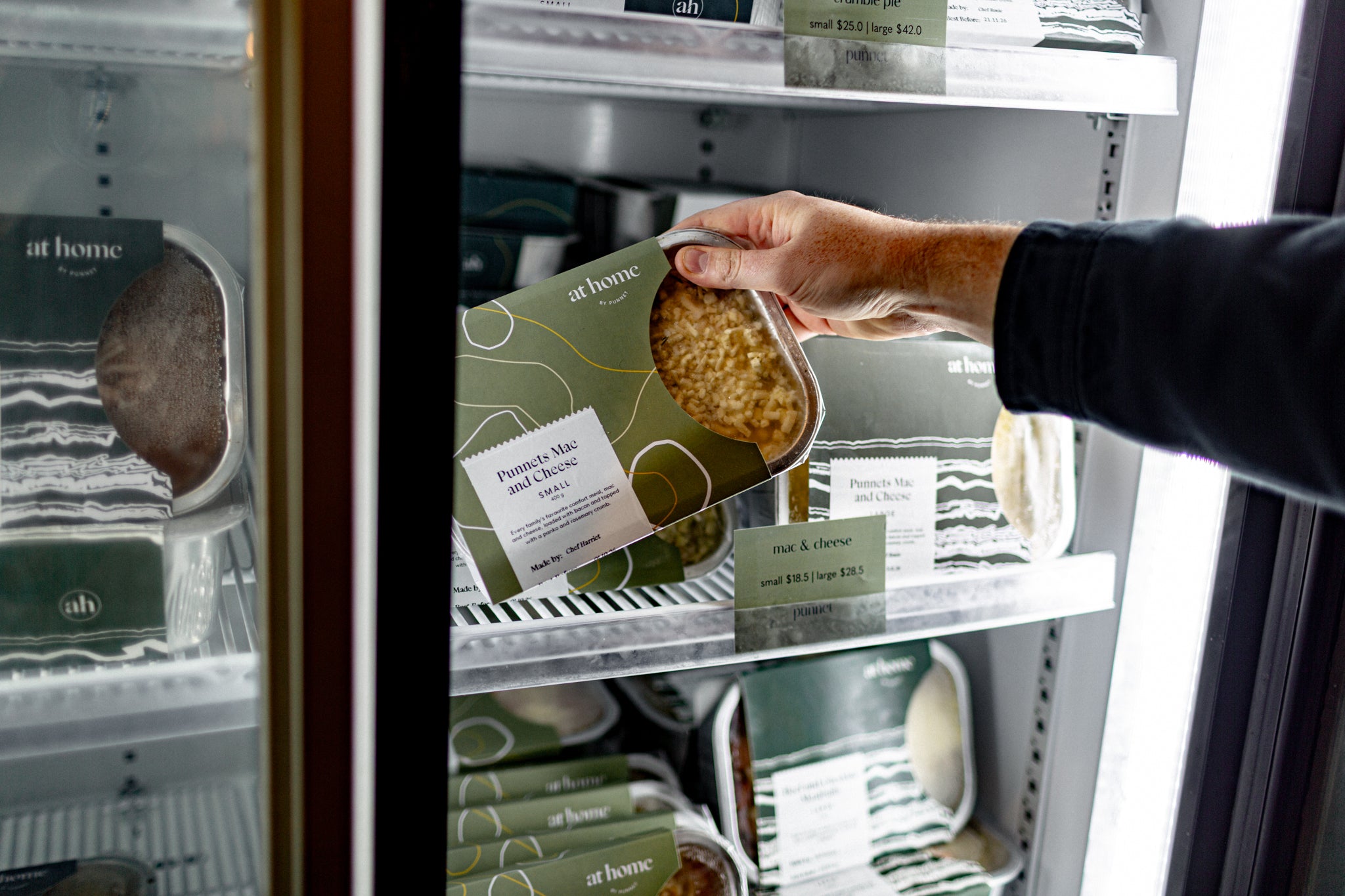 A hand reaches into a refrigerator shelf holding Punnets Mac and Cheese at home meal