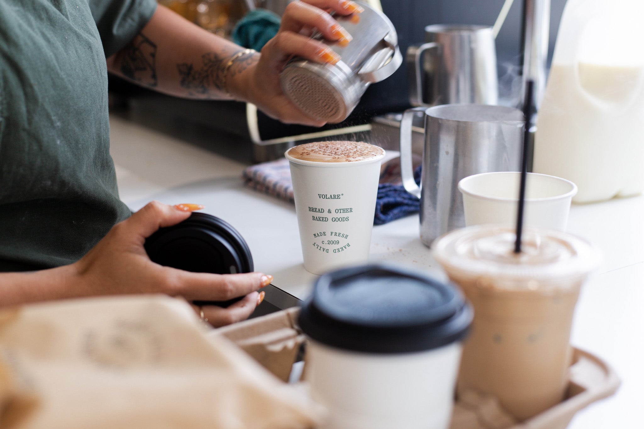 Barista sprinkling chocolate on a coffee at Volare Bread Main Bakery store.