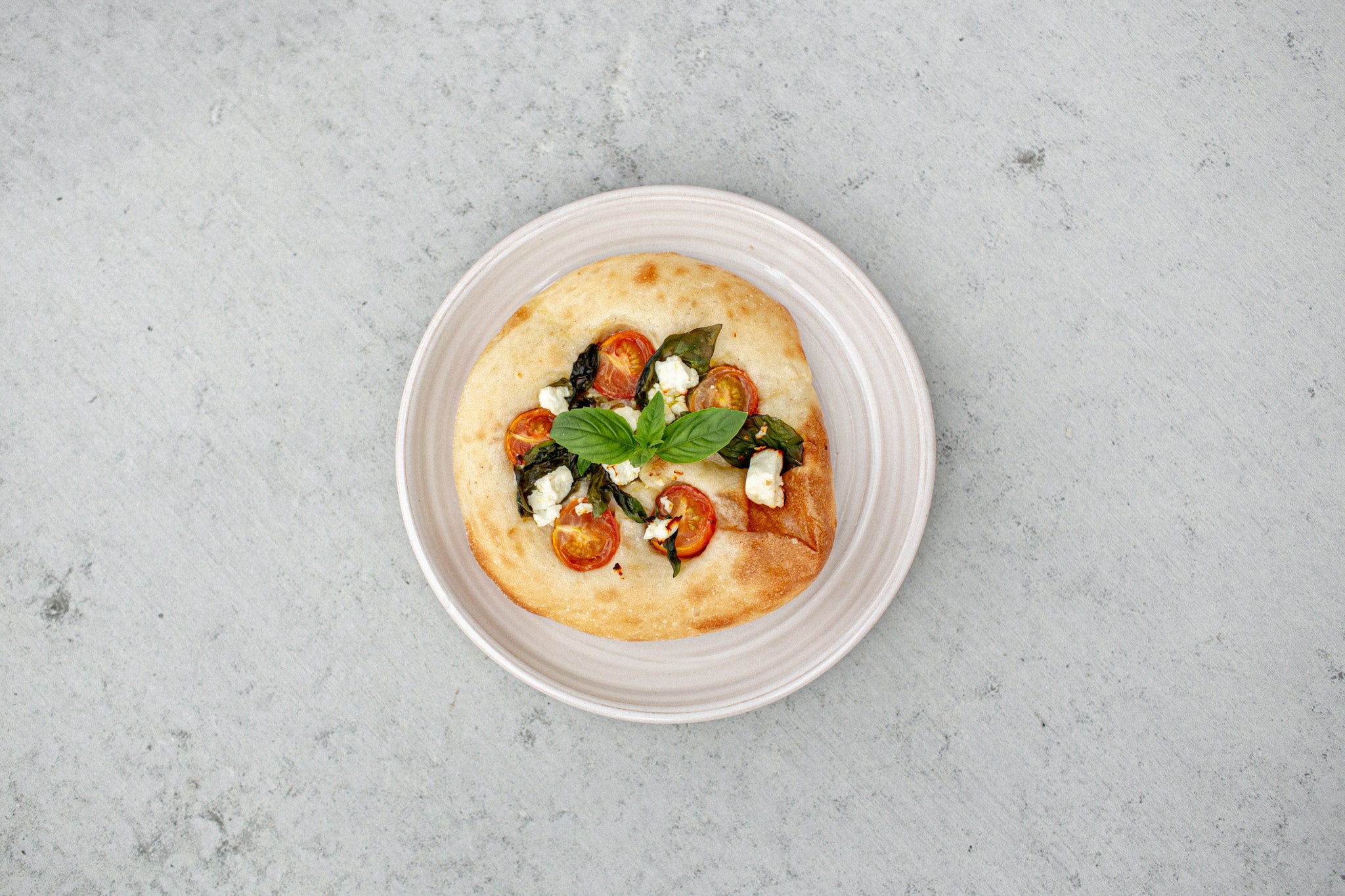 Focaccini with cherry tomatoes, feta, and basil on a white plate. 