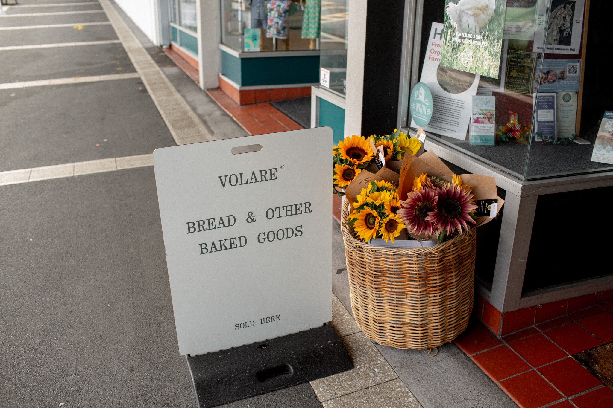 Volare Bread & Other Baked Goods sign with a basket of flowers in front of a store entrance.