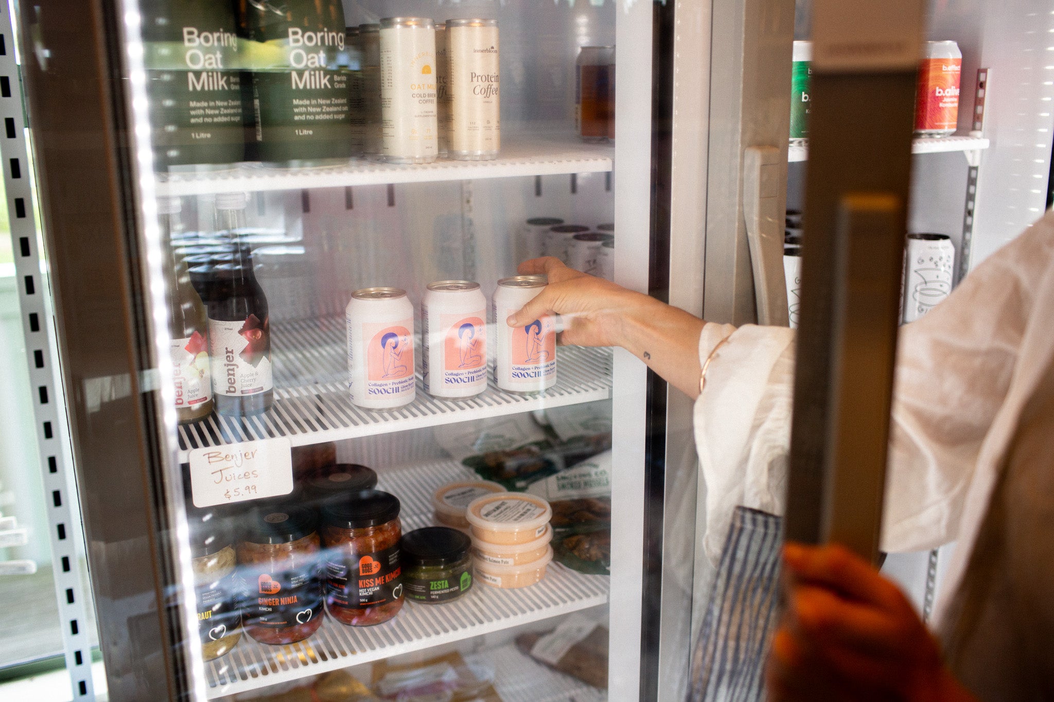Person reaching into a refrigerator stocked with various products including cans and bottles.