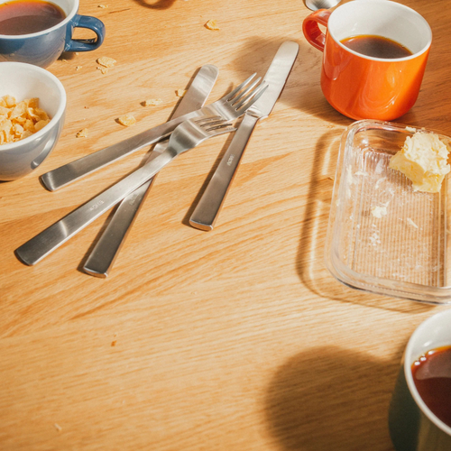 Wooden table with coffee cups, butter dish, and utensils