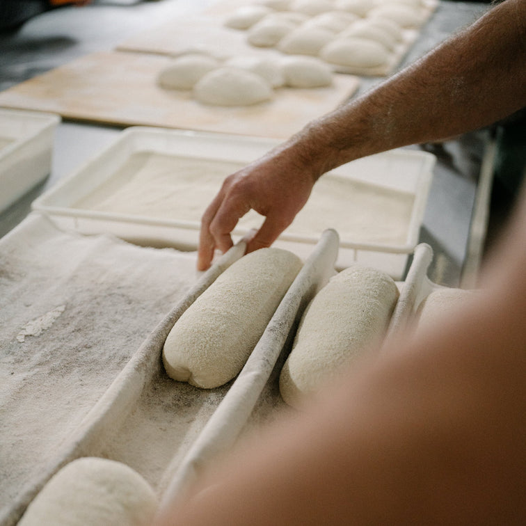 Person handling dough balls on a baking tray in a kitchen setting