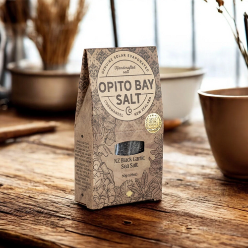 Opito Bay NZ Black Garlic Sea Salt packaging on a wooden surface with a blurred background