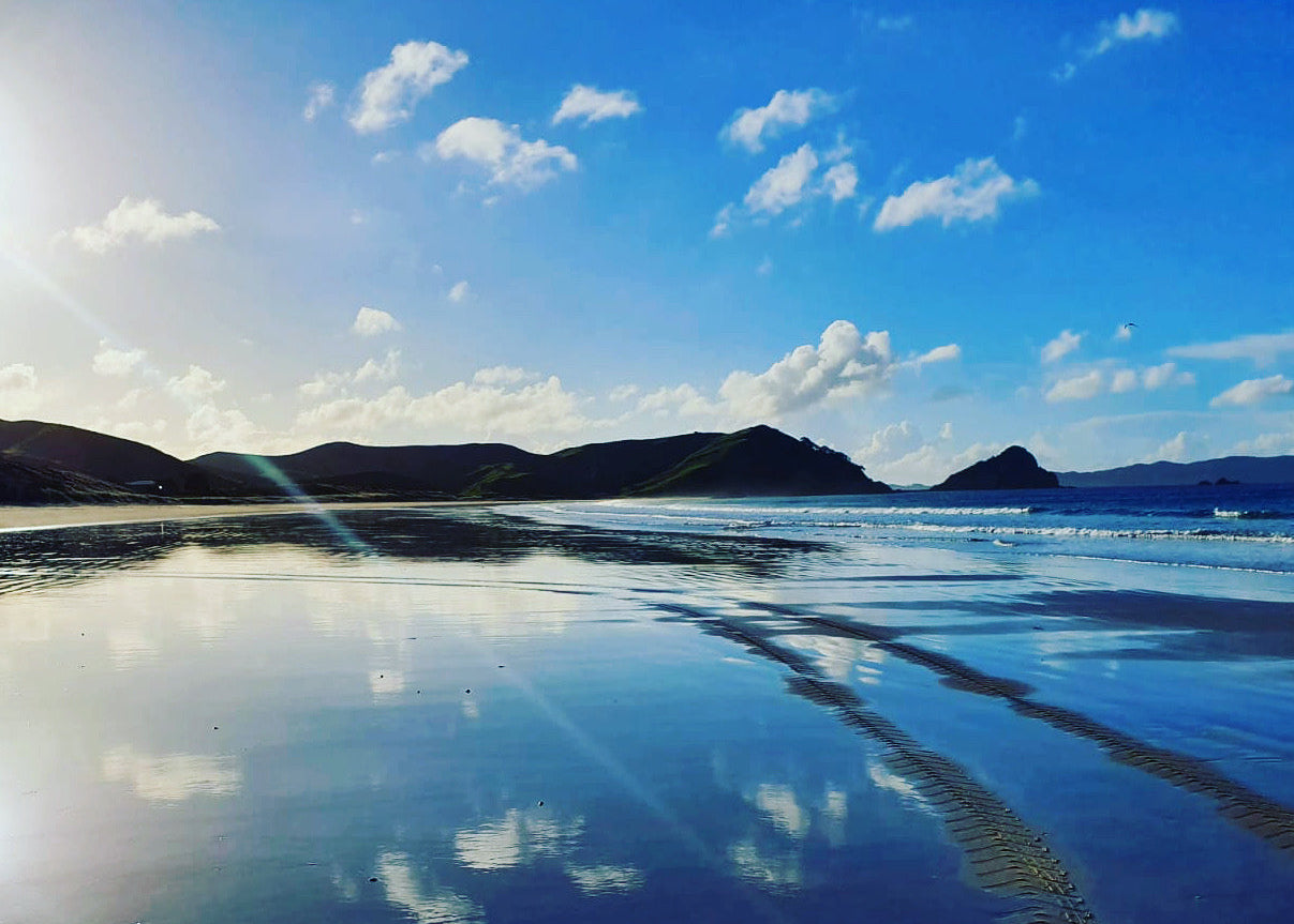 Opito Bay Beach with clear blue water and sky, reflecting clouds