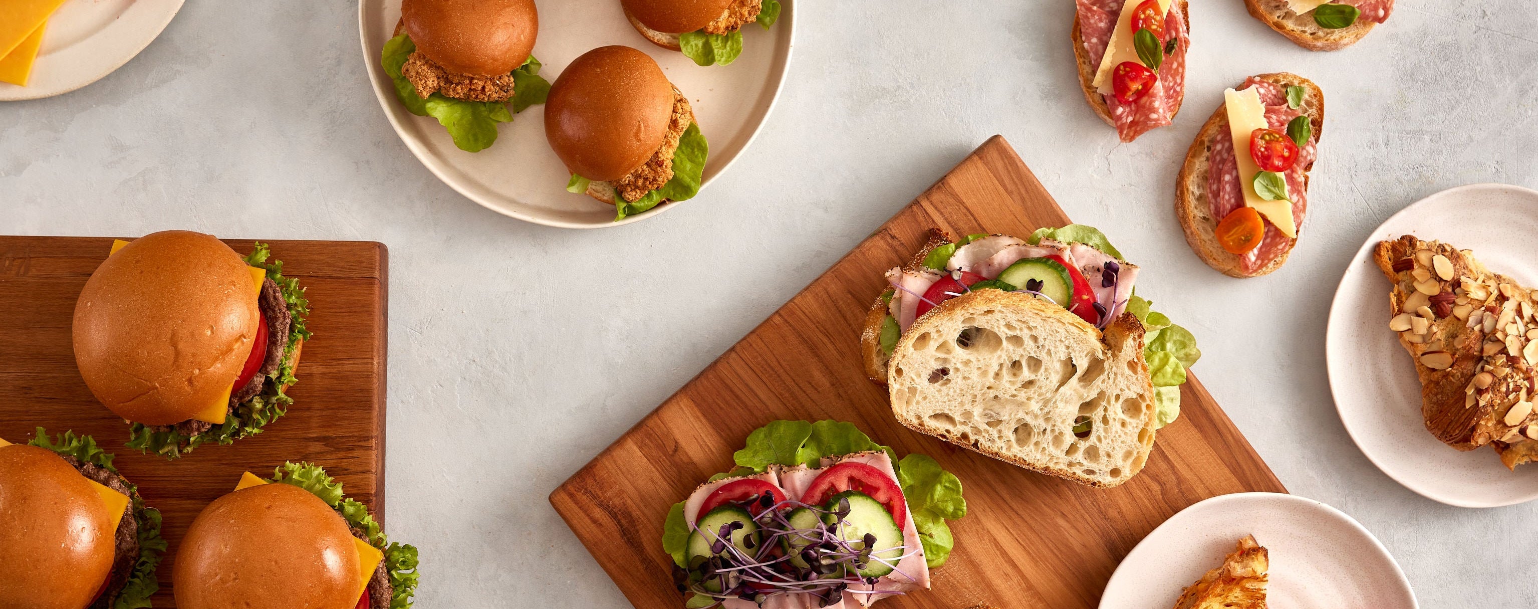 Assorted sandwiches and small plates of food using Volare products on a light gray surface with a wooden cutting board.