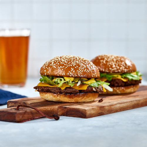 Two Volare burgers on a wooden board with two glasses of beer in the background.