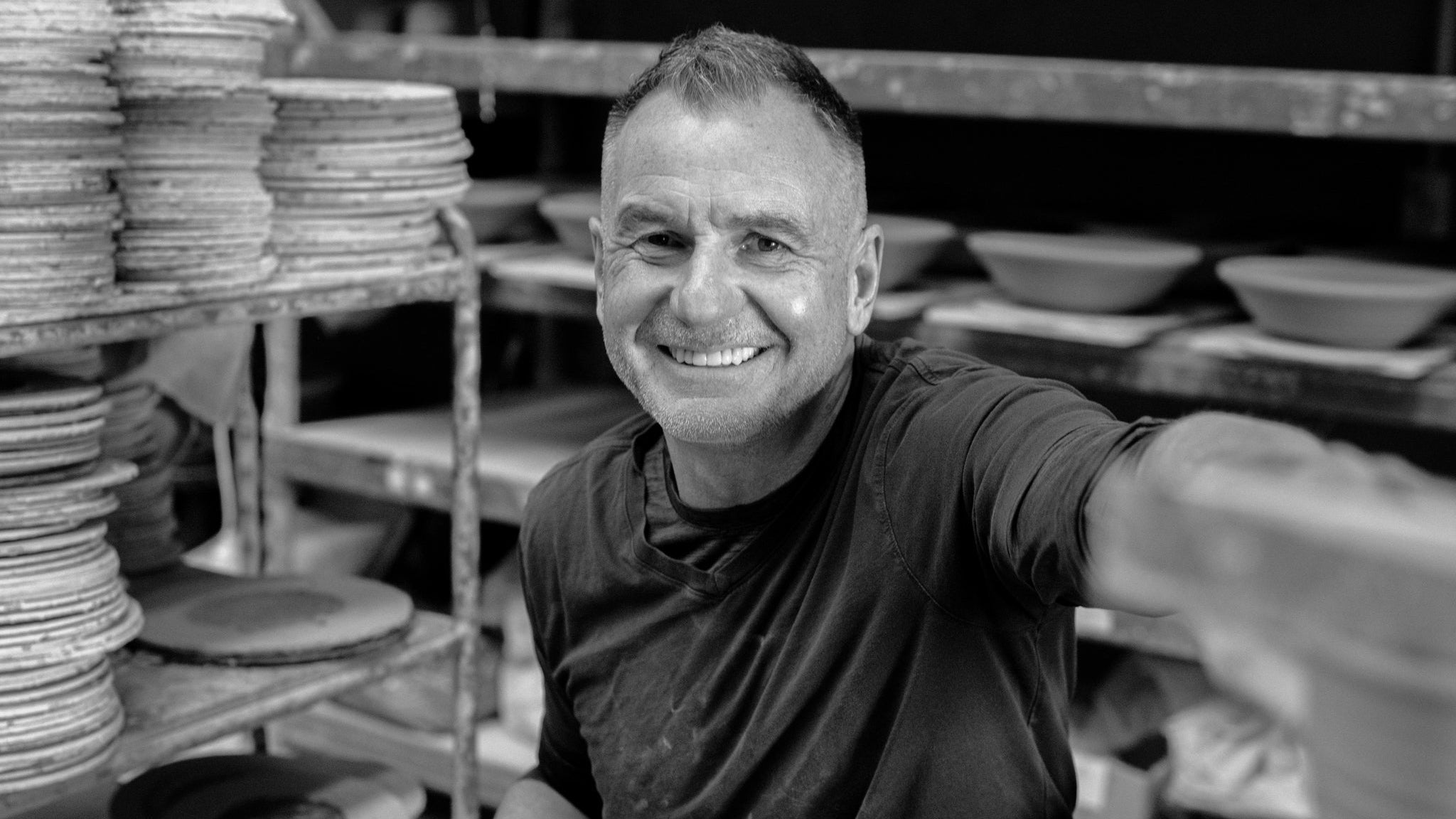 Tony Sly sitting among ceramic plates and pottery in a workshop